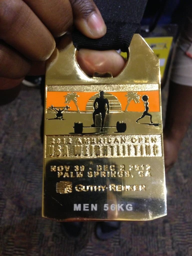 A hand holding a gold medal engraved 2012 American Open, USA Weightlifting, Palm Springs, California