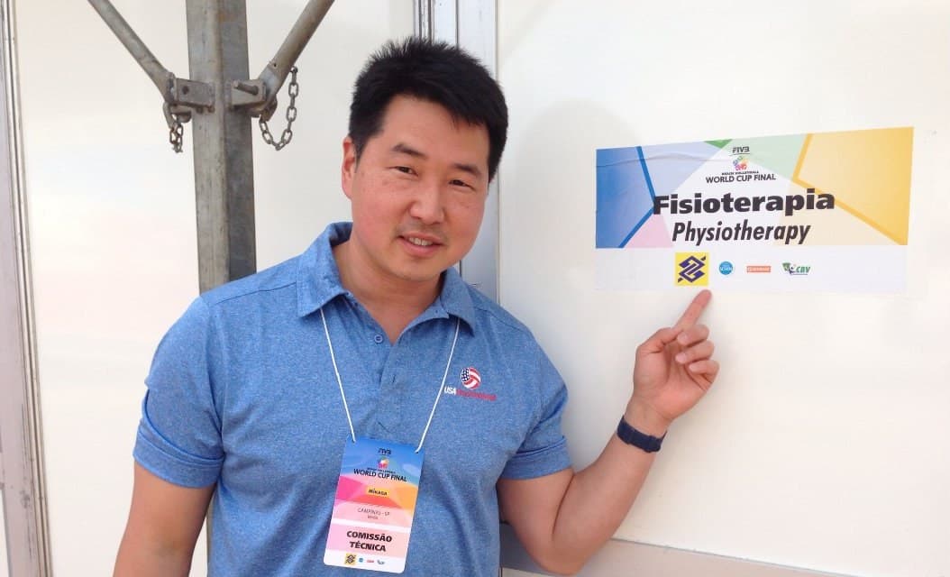 Dr. Koh, wearing an event credential, pointing at a sign reading Fisioterapia, Physiotherapy