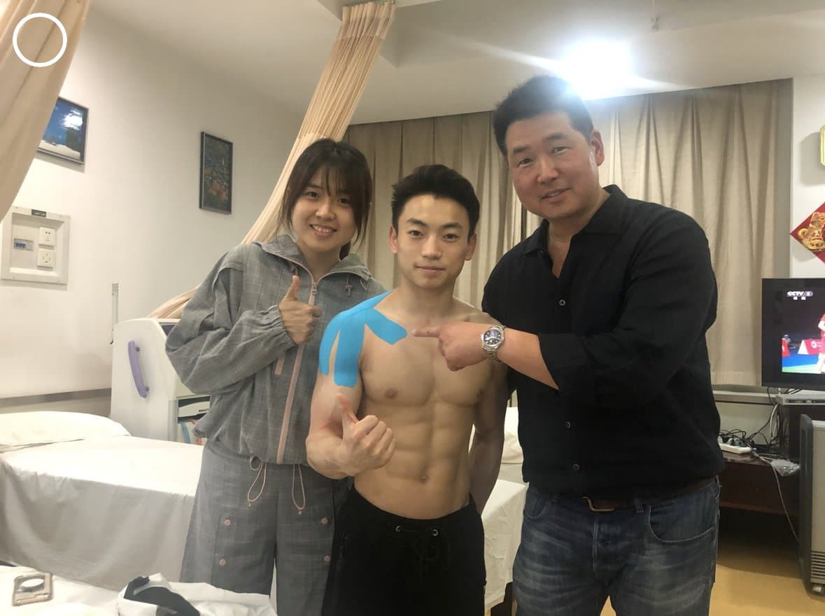Dr. Koh with a gymnast who has blue kinesiology tape on his shoulder, and a colleague