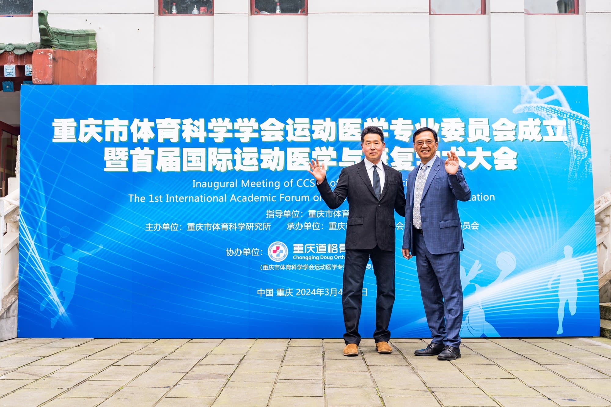 Dr. Koh and a host in suits standing in front of a large blue forum banner with Chinese and English text
