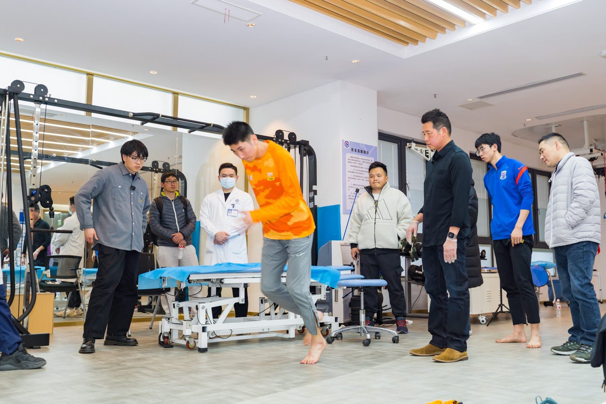 Dr. Koh and a group of clinicians watching an athlete in an orange shirt perform a movement on a treatment table