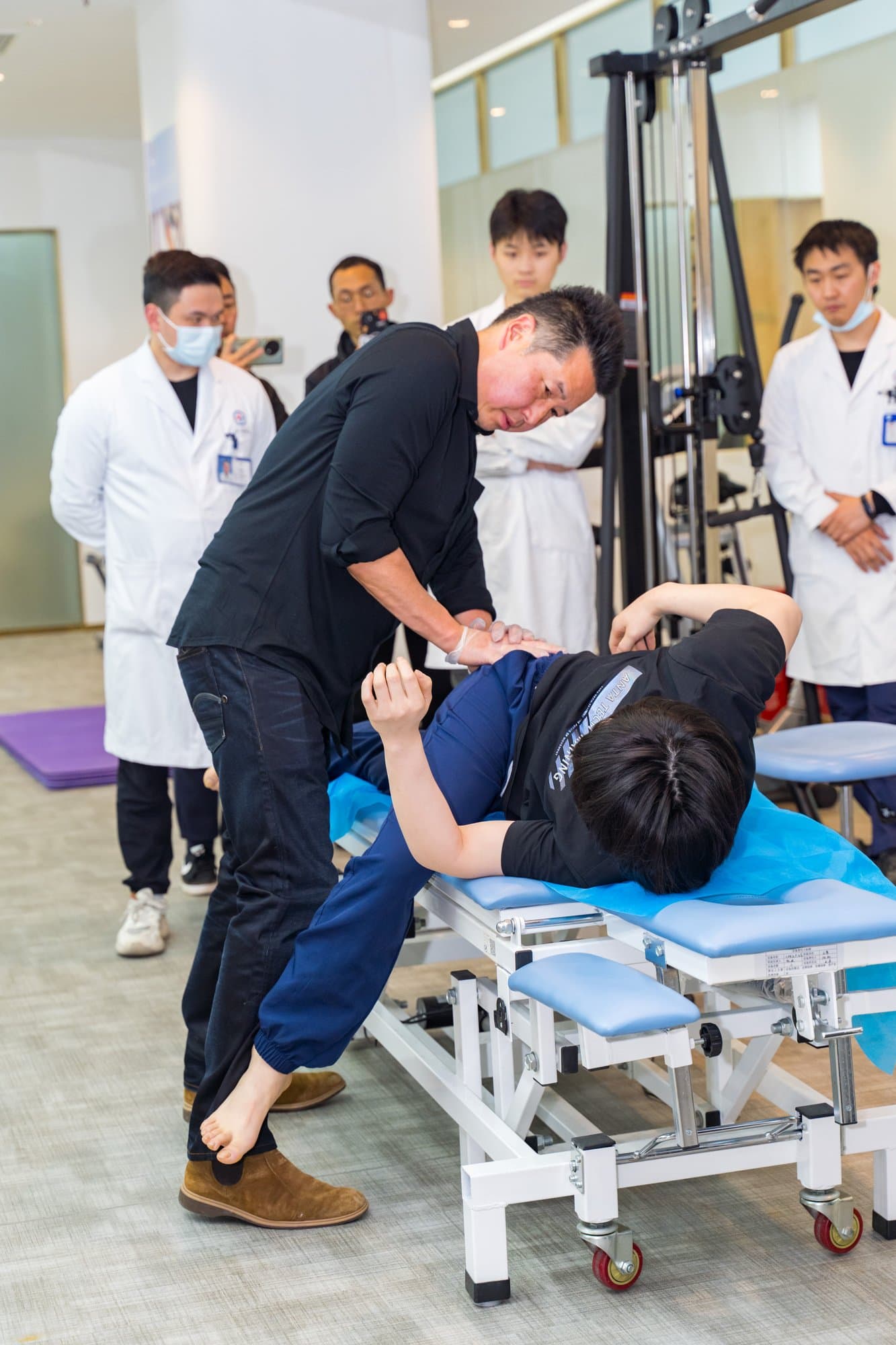 Dr. Koh demonstrating a manual technique on a person lying on a treatment table while clinicians in white coats watch