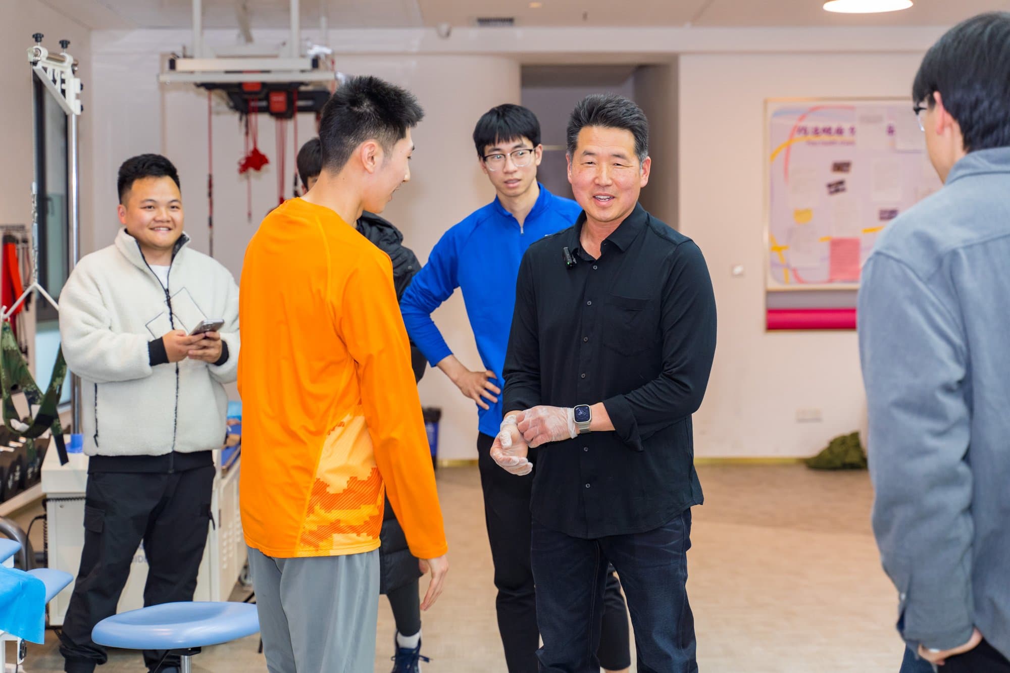 Dr. Koh, wearing treatment gloves, standing with a group of athletes in a rehabilitation gym