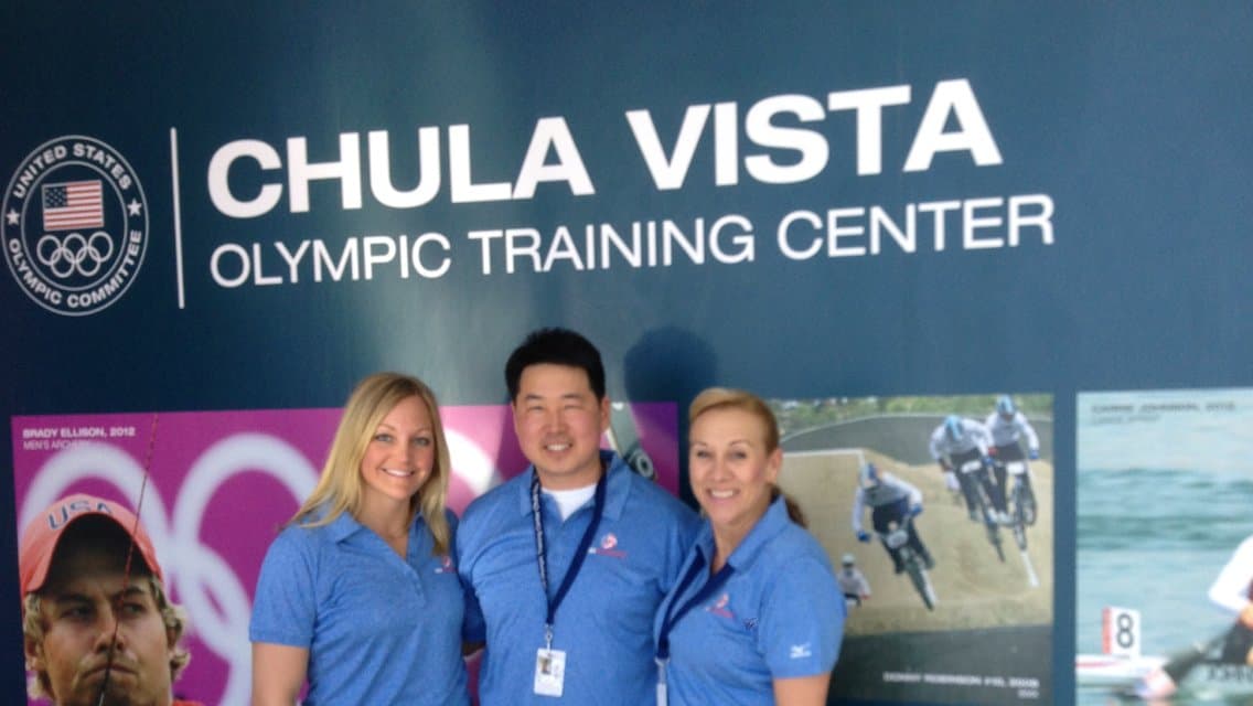 Dr. Koh and two colleagues in blue staff shirts standing under a Chula Vista Olympic Training Center sign
