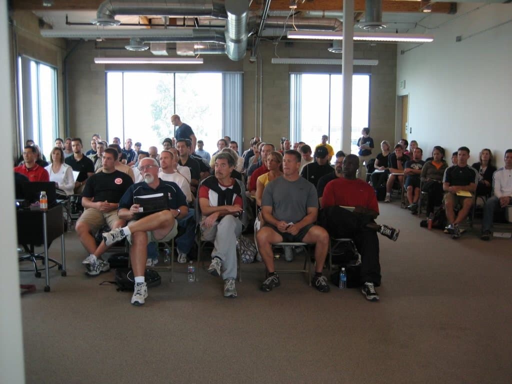 A large seated audience of course attendees in a bright room
