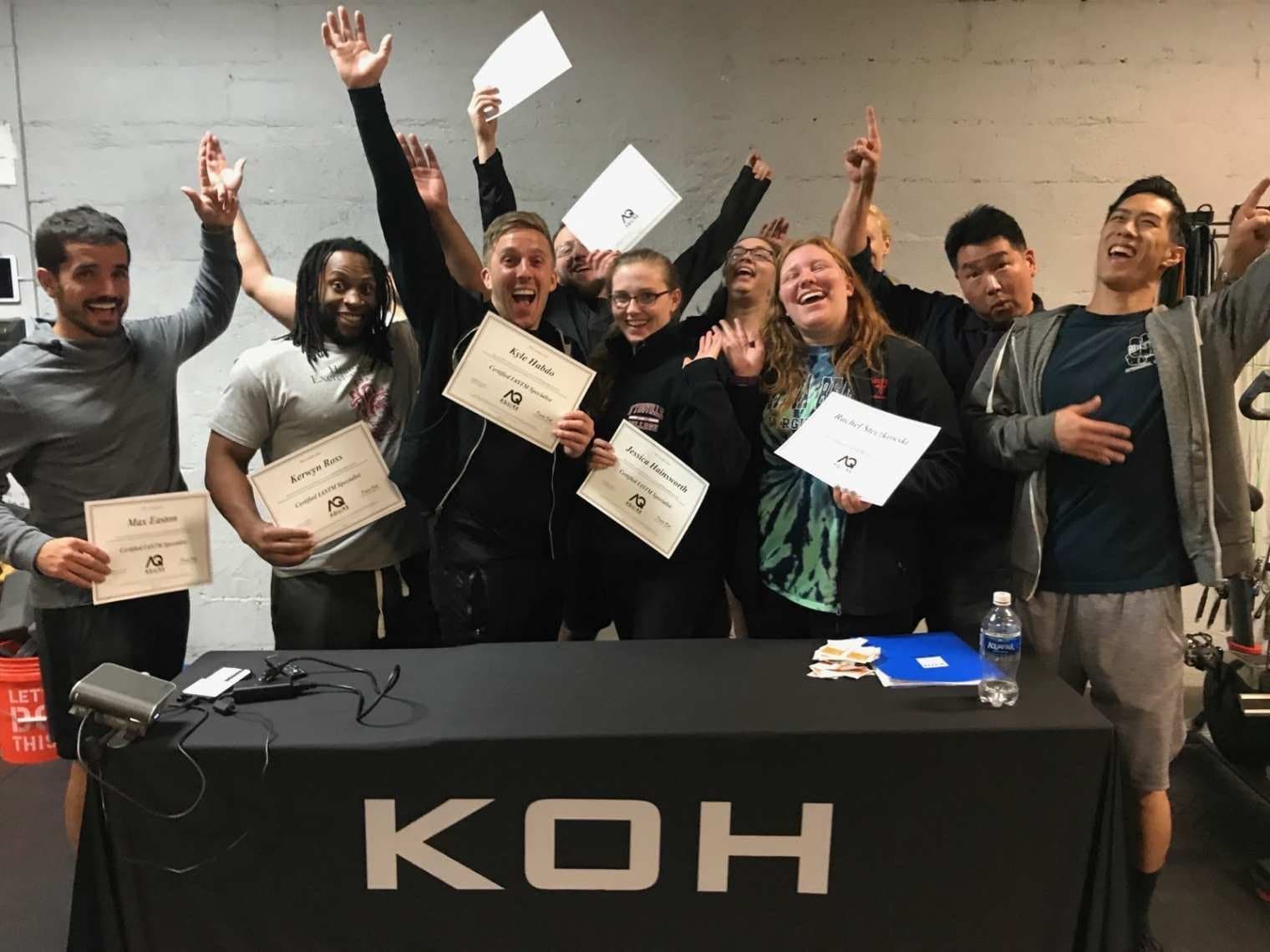 Course attendees holding certificates and cheering behind a table with a KOH banner