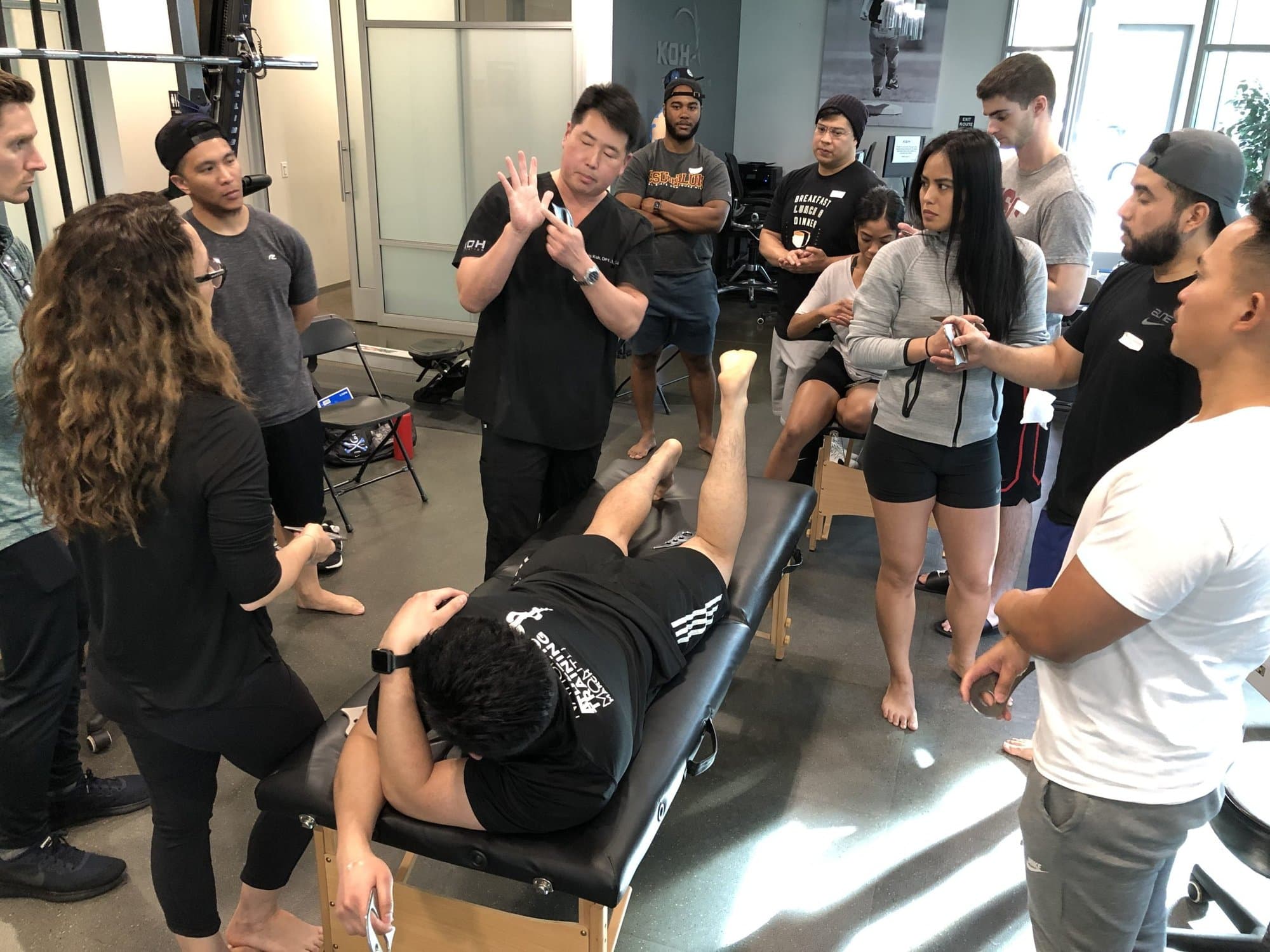 Dr. Koh explaining a technique to attendees gathered around a treatment table