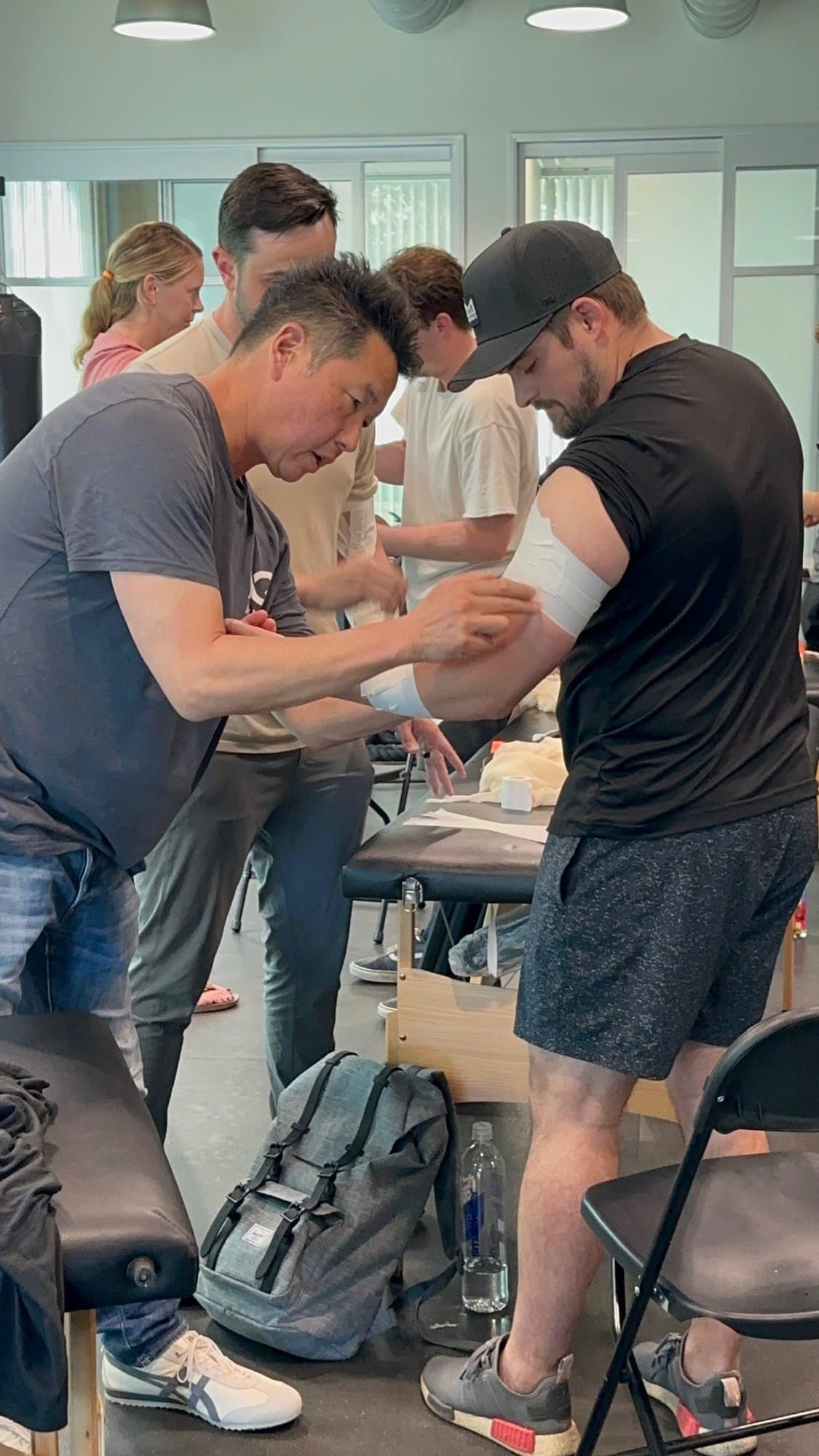 Dr. Koh applying tape to an attendee's upper arm during a course