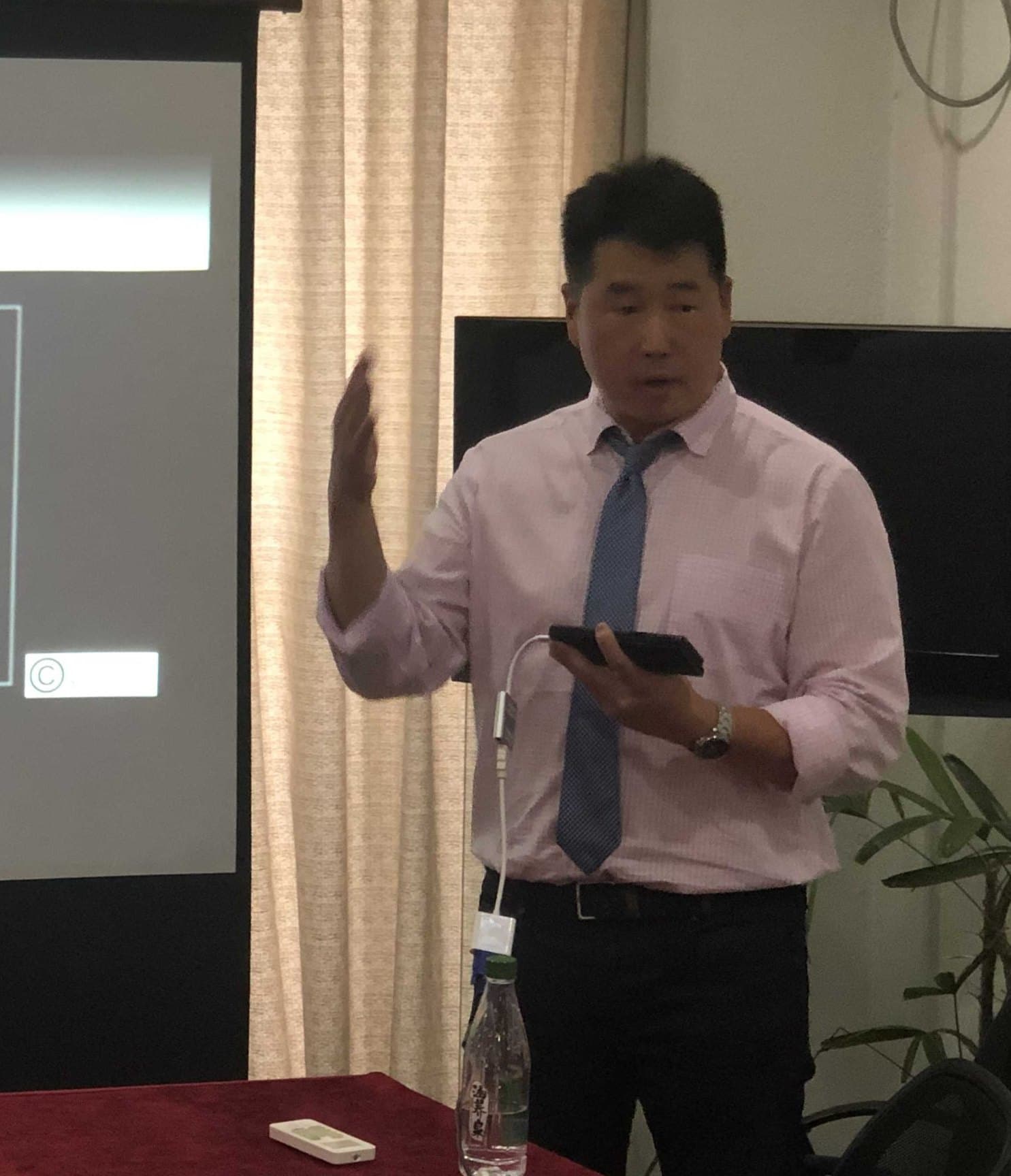 Dr. Koh in a shirt and tie, teaching beside a projector screen