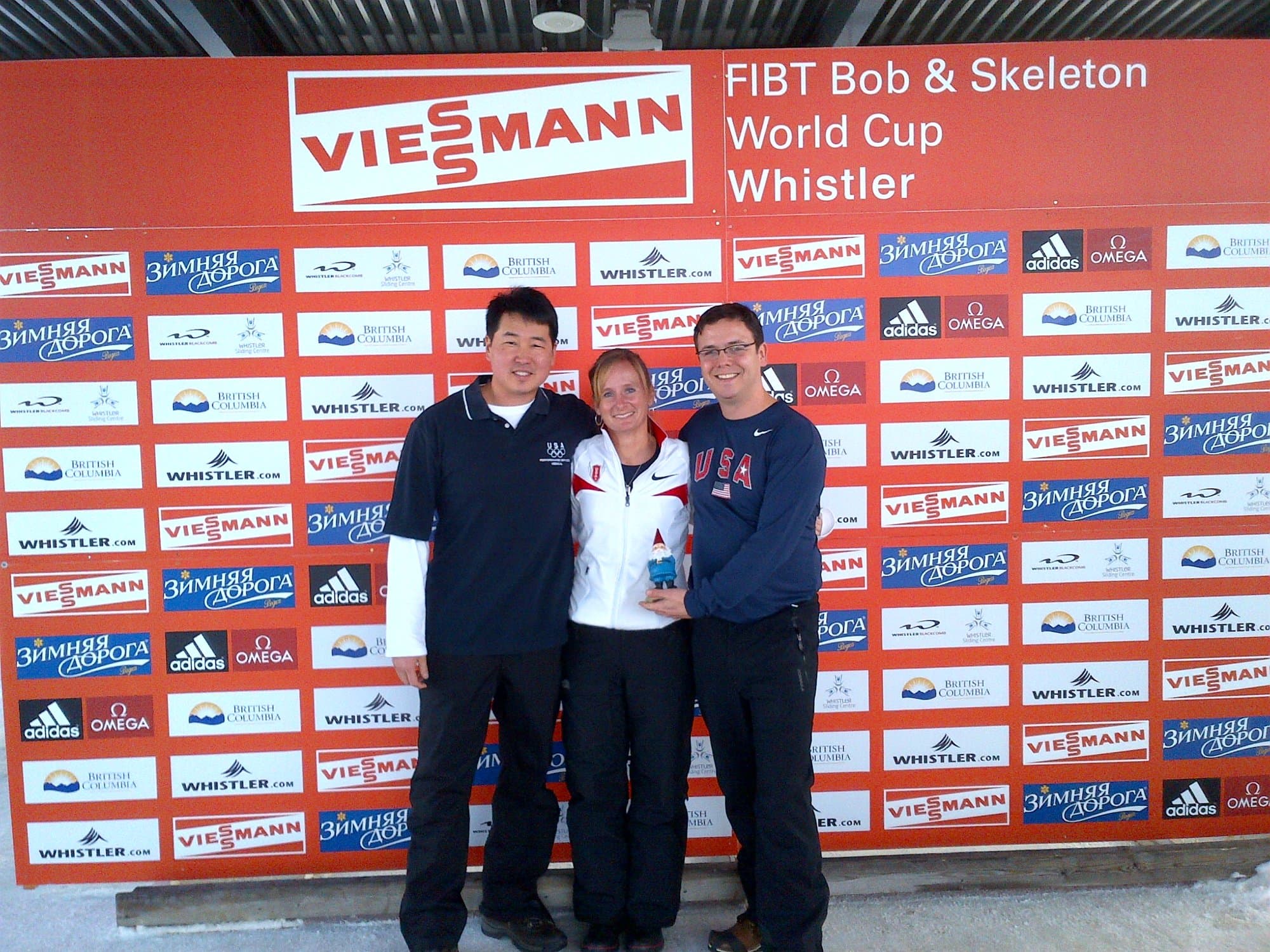 Dr. Koh and two team members in front of a FIBT Bob and Skeleton World Cup Whistler backdrop