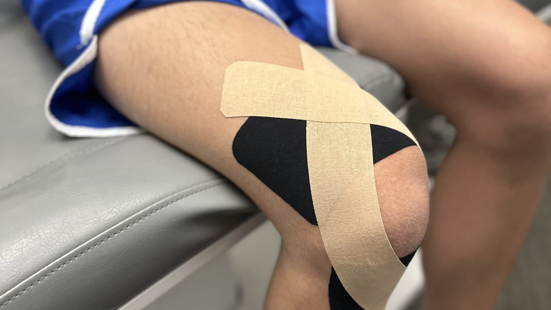 Beige and black kinesiology tape applied in a crossing pattern around a knee