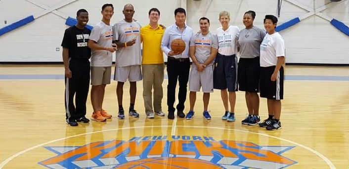 Dr. Koh holding a basketball at center court with nine members of the sports medicine staff, standing on the New York Knicks logo