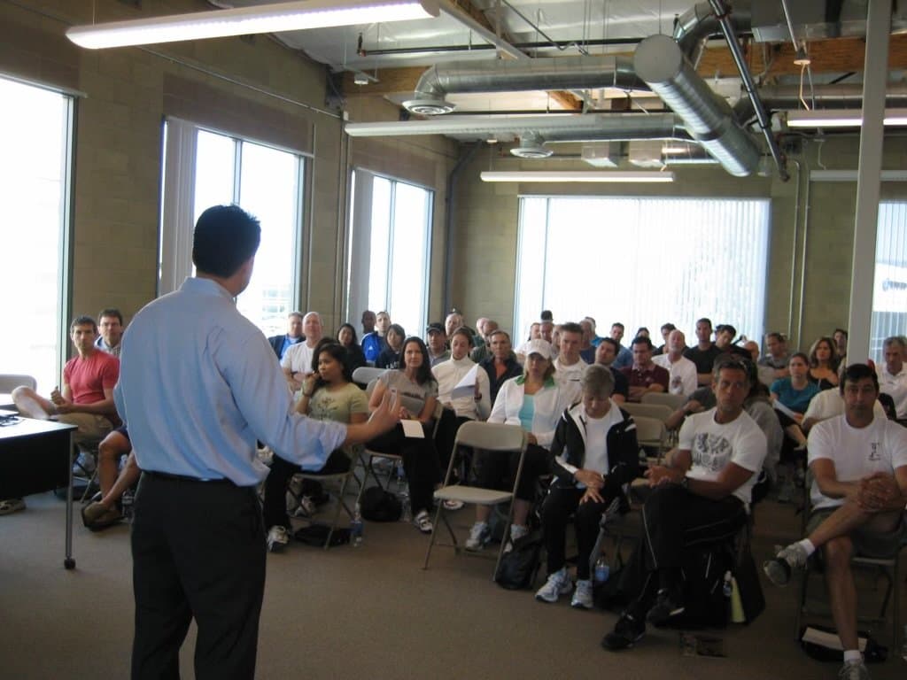 Dr. Koh, seen from behind, lecturing to a full room of seated attendees