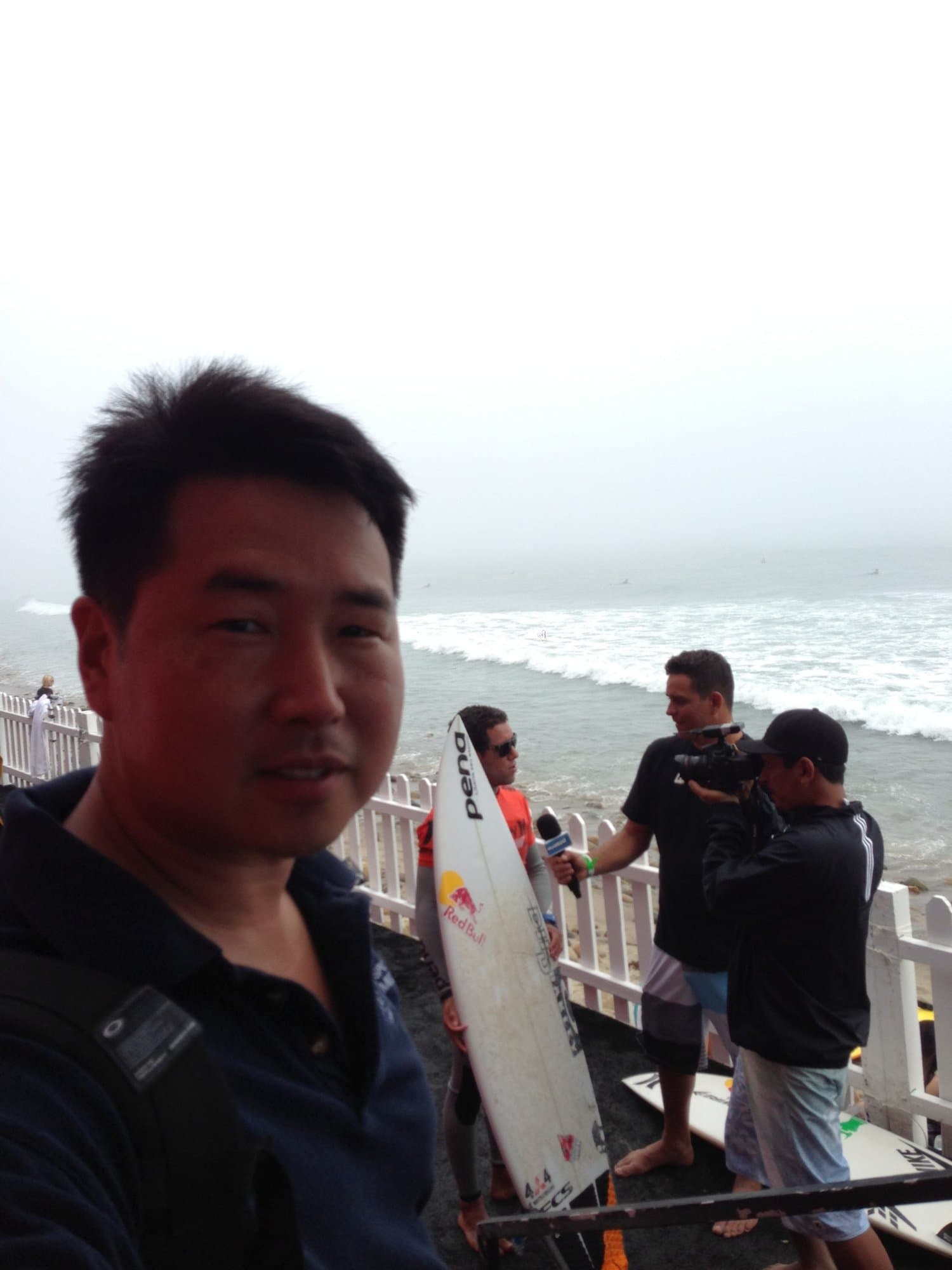 Dr. Koh on a foggy beach with a surfer being interviewed on camera behind him
