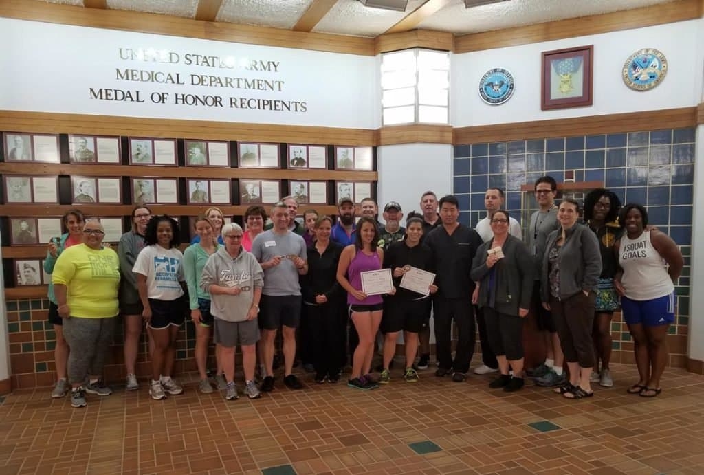 A large group of course attendees holding certificates in front of a wall reading United States Army Medical Department, Medal of Honor Recipients