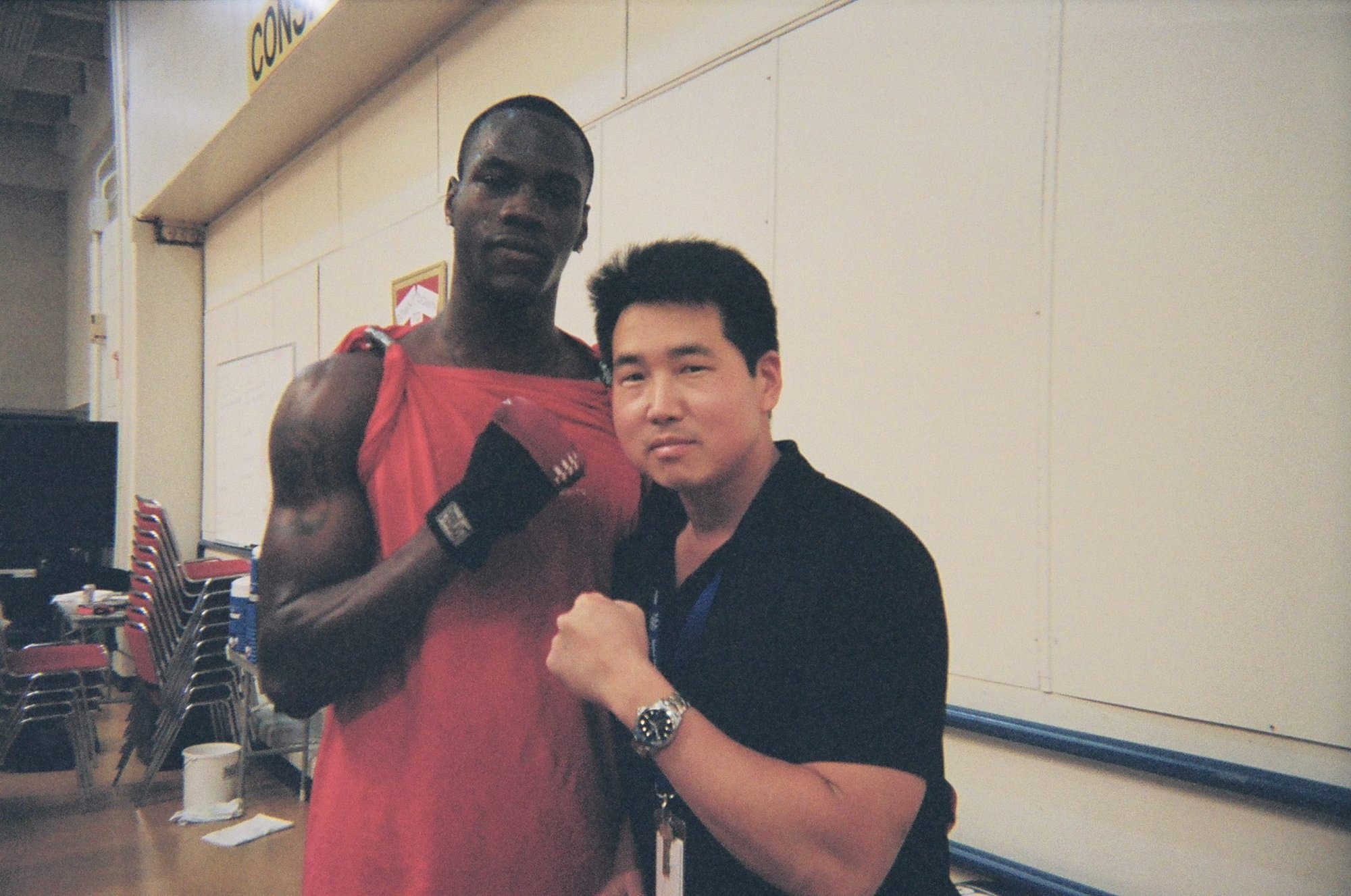 Dr. Koh standing beside an athlete in a red singlet and hand wraps at a competition venue